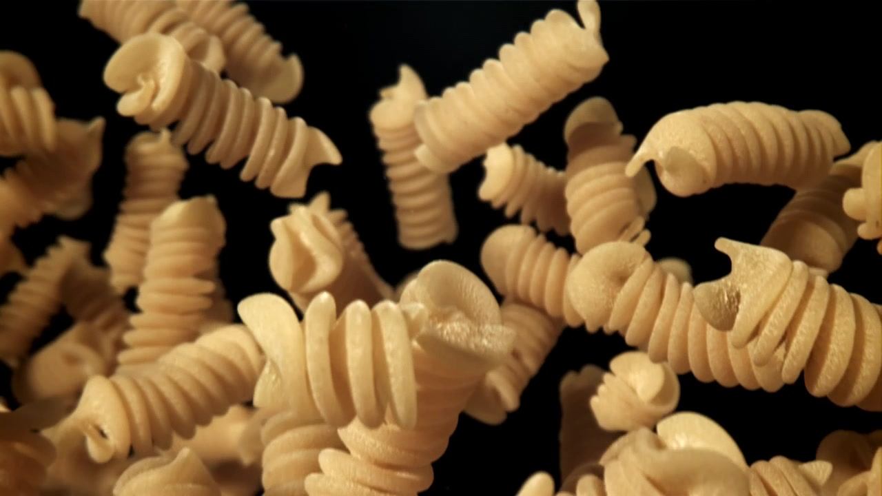 Primo piano di pasta fusilli cruda che cade al rallentatore.