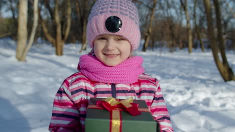 Joyful-little-smiling-kid-girl-holding-Christmas-present-gift-box-in-winter-park,-xmas-eve-holidays