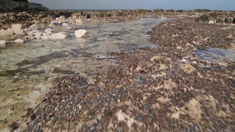 Rocky-low-angle-aerial-drone-shot-passing-above-pools-of-shallow-sea-water-in-rock-crevices