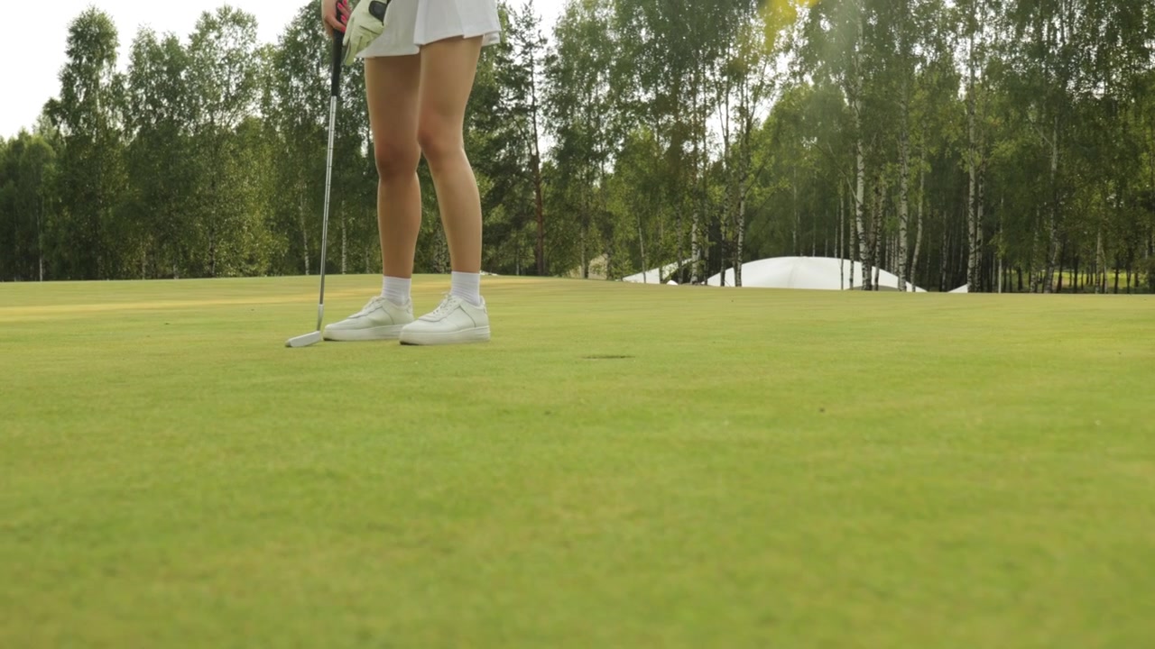 Primo piano di una donna che imbuca e recupera una pallina da golf sul green