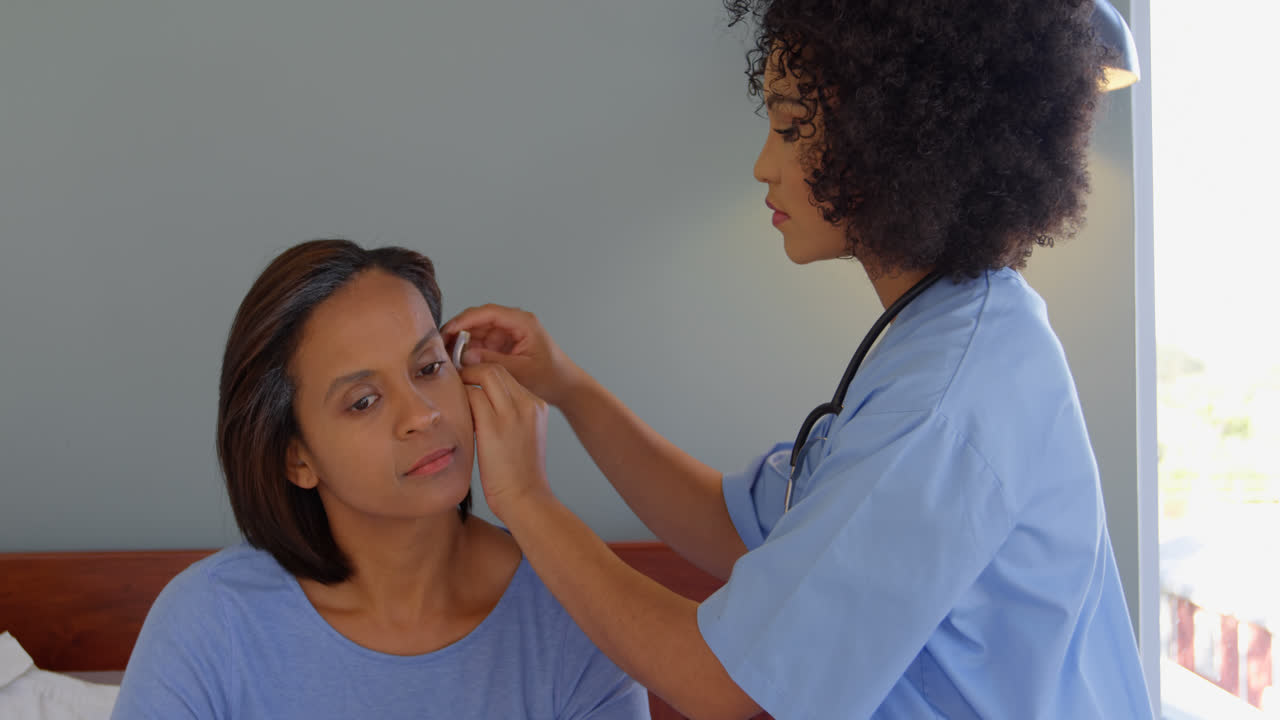 Mixed race female doctor inserting a hearing aid machine on womans ear at home 4k
