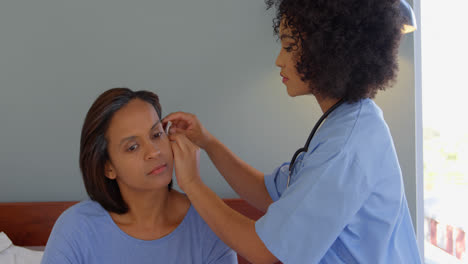 mixed race female doctor inserting a hearing aid machine on womans ear at home 4k