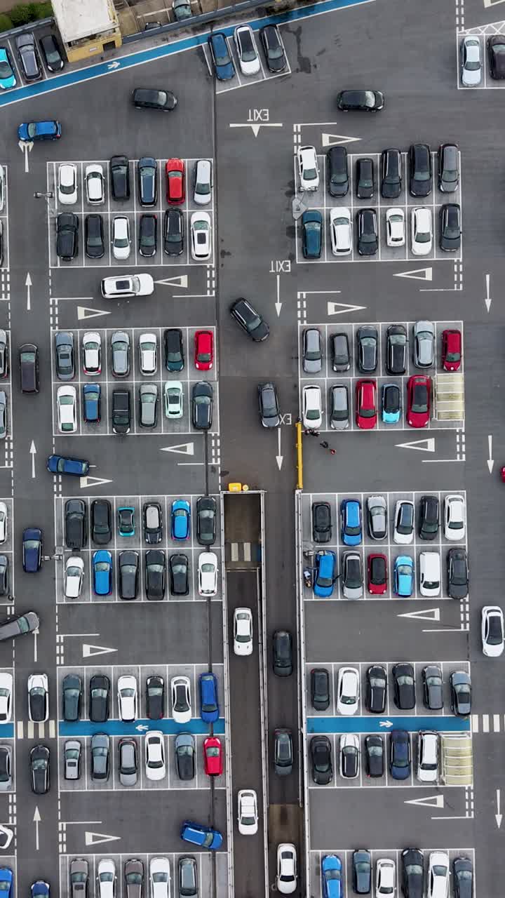 Vertical top-down drone timelapse of Water Garden Harlow, UK, car park. Cars drive around busy car park, with lower level visible, and traffic flow on main road at top, capturing urban movement