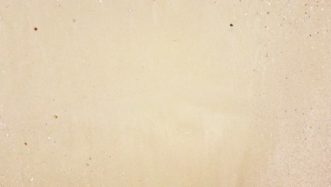 bird's eye view of ocean waves crashing against an empty sand beach from above
