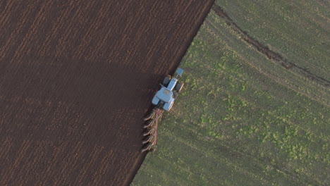 Aerial-view-of-a-farm-tractor-ploughing-a-field-in-Aberdeenshire-on-a-sunny-day,-Scotland