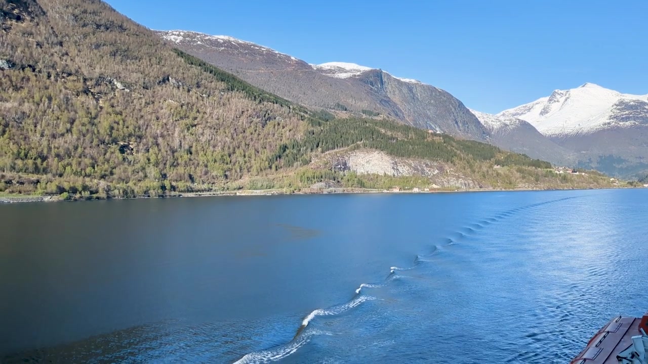 Vista dal balcone di una nave da crociera su un fiordo norvegese con la scia della nave e montagne innevate - Olden, Norvegia.