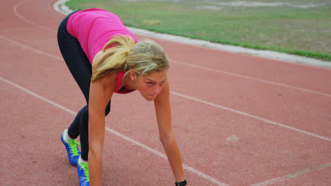 vista frontal de una atleta caucásica tomando la posición inicial y corriendo en una pista en un evento deportivo