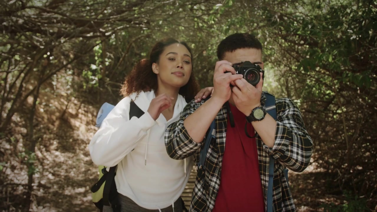 Homem levantando DSLR para fotos em trilha, causando falhas em "BOAS VIBRAÇÕES", que se estabilizam enquanto mulher alcança a alça.
