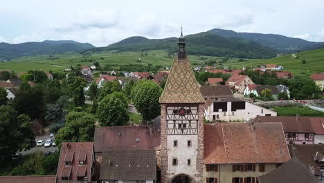 An-upward-jib-shot-aerial-footage-of-the-clock-tower-while-revealing-the-houses,-the-roads,-the-grasslands,-and-the-whole-village