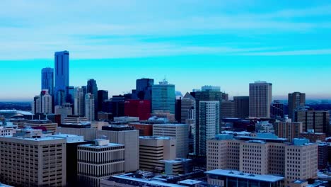 winter snow covered congested skyscraper buildings post modern architecture in downtown edmonton where smoke stacks are blowing in a freezing cold blue hour of a day with some clouds and blue horizon