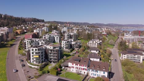 multi-unit residential apartments with green rooftop in wädenswil, switzerland. sunny day with blue sky in spring. lake zurich in background. aerial wide shot.