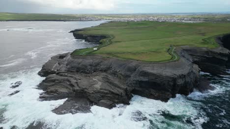 Olas-Rompiendo-A-Lo-Largo-De-Los-Acantilados-De-Kilkee-Con-El-Pueblo-Costero-En-El-Fondo,-El-Condado-De-Clare-En-Irlanda