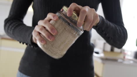 woman picking up a jar with brown almond flour and open it in the kitchen