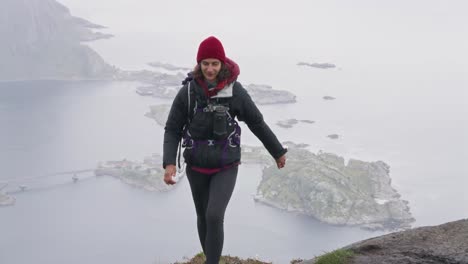 an athletic woman arriving at the top of reinebringen hike with a view of hamnøy in the background, reine, lofoten islands, norway