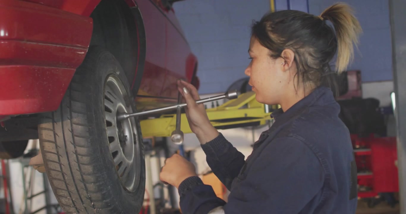 Vertical video: Female mechanic inserting breaker bar, loosening lug on lift with galaxy overlay