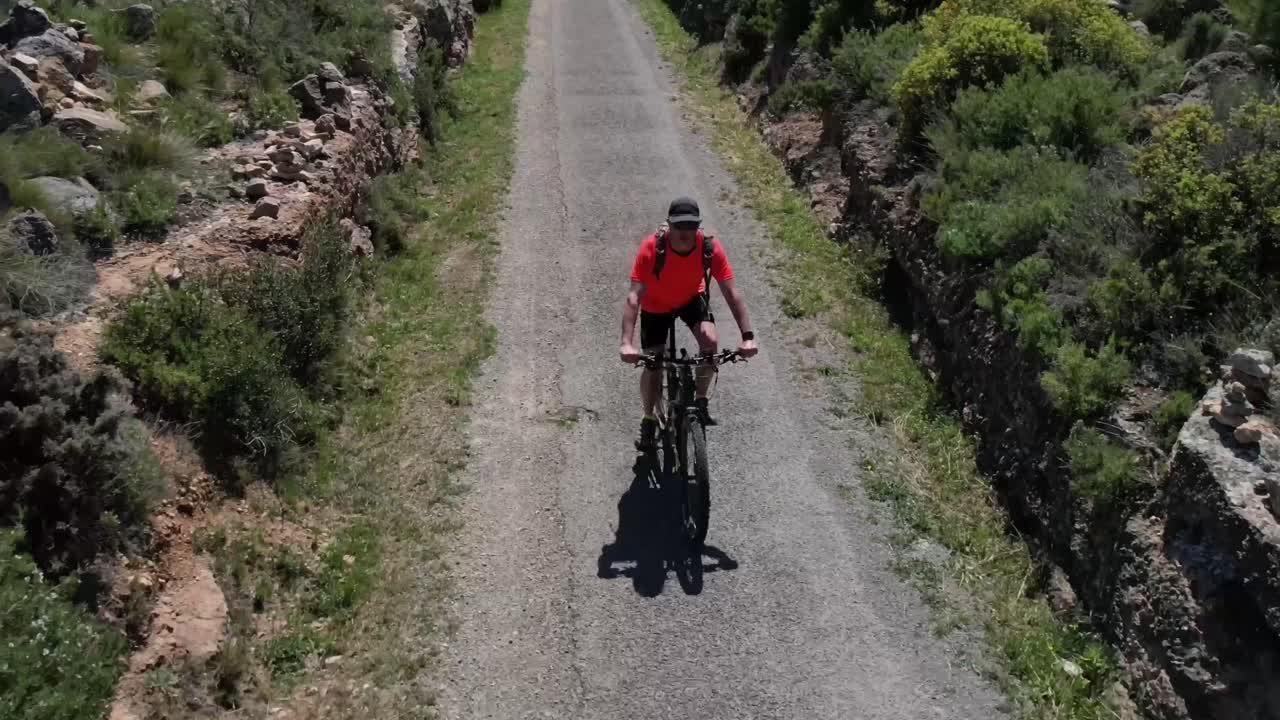 Uomo di mezza età con un cappellino, occhiali da sole e una maglietta arancione in sella a una MTB che percorre un vecchio sentiero ferroviario