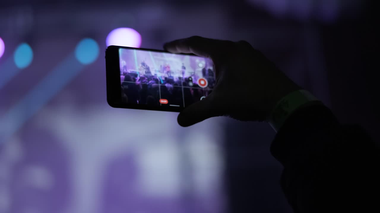 silueta de las manos tomando fotos o grabando video de un concierto de música en vivo con un teléfono inteligente. iluminación de escenario colorida y brillante