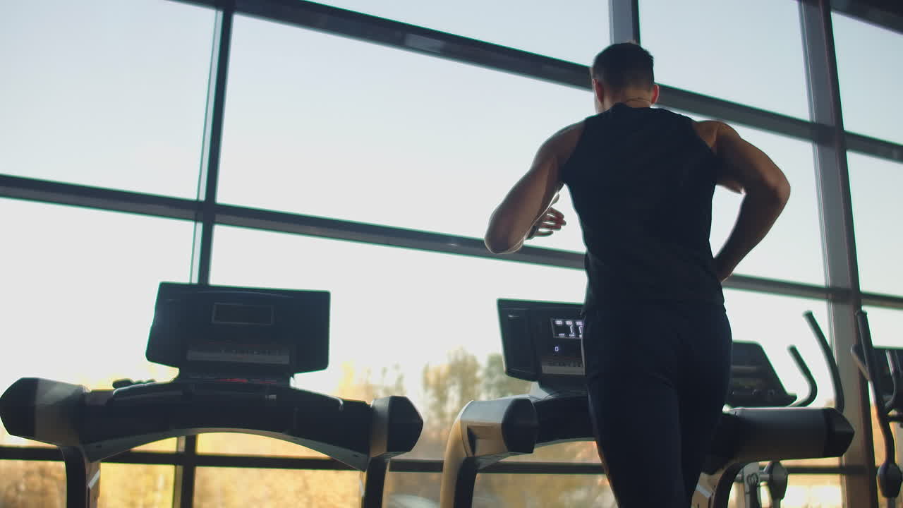 젊은 운동선수 남녀가 스포츠 체육관에서 트레드밀에서 운동하고 달리고 있습니다. 큰 파노라마 창문 근처의 느린 동작