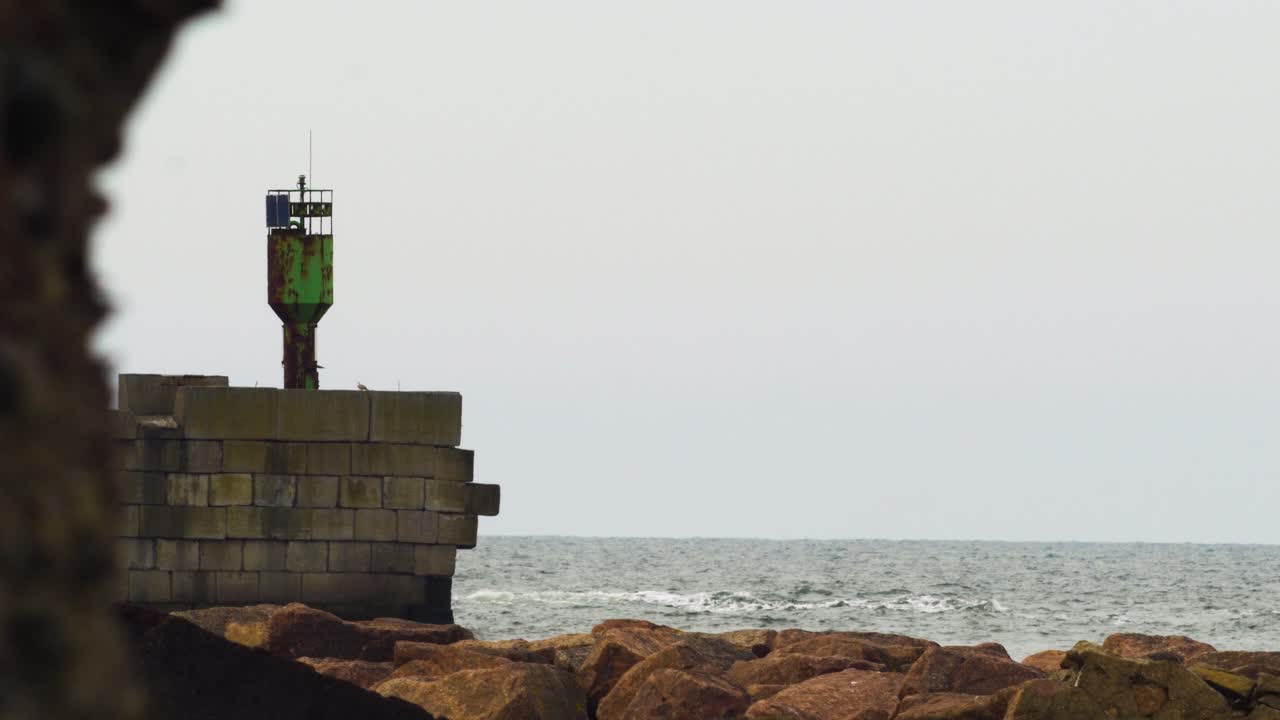 리파자 항구를 떠나는 주황색 항구 파일럿 배는 석조 부두, 녹색 항구 항법 표지, 발트해, 흐린 봄날, 멀리서 중간 샷