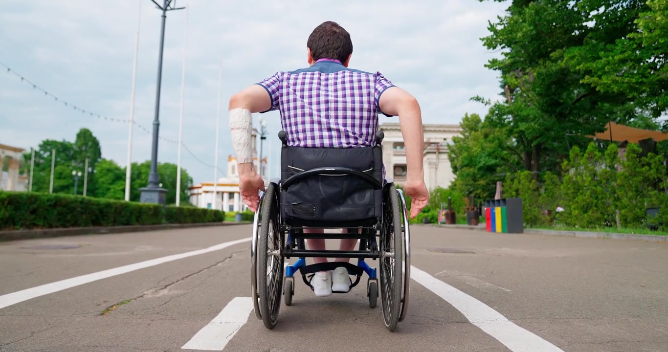 Rear View of Man in Wheelchair Moving Along Park Road