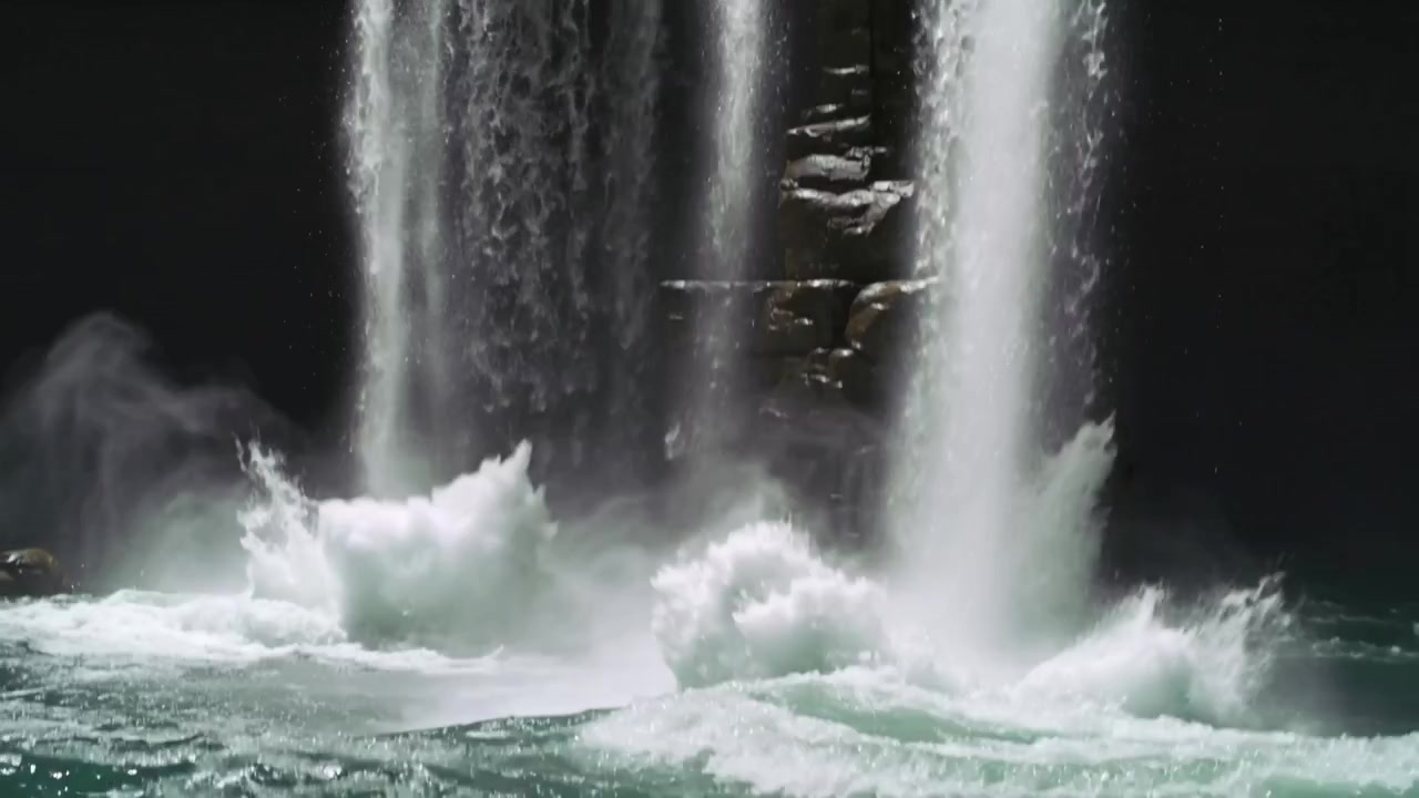 溢れ出る滝のカーテンが崖の縁の上の中央の岩の柱を現し、立ち上る水しぶきを発生させている。