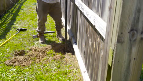 man using a prybar to dig out a post hole