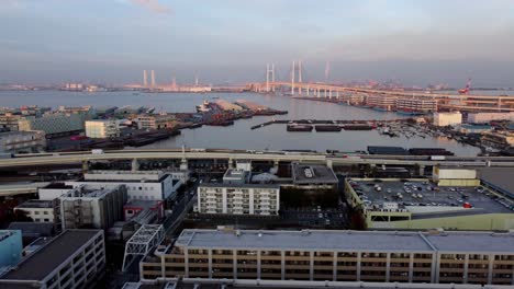 A-coastal-cityscape-at-dusk-with-bridge-and-industrial-port,-aerial-view