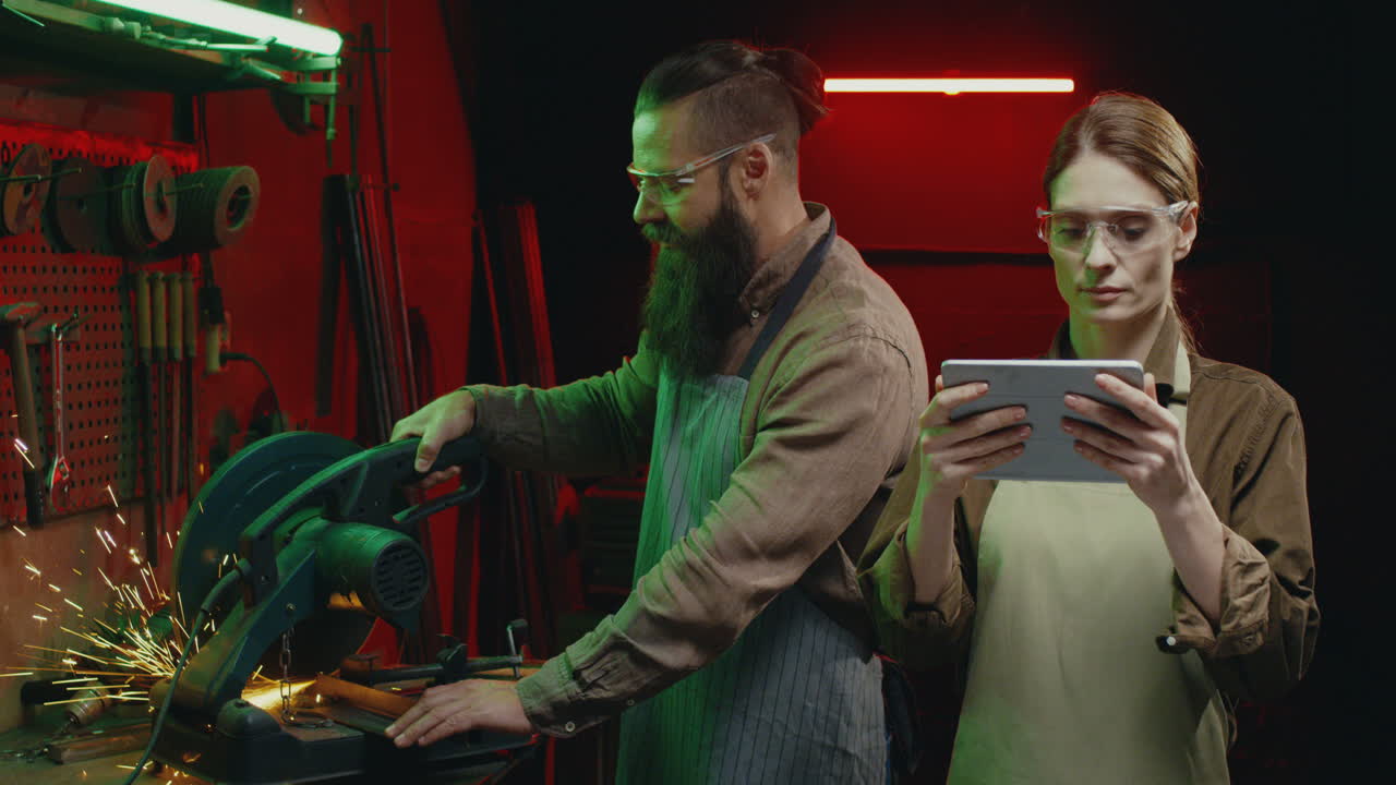 작업장에서 태블릿을 두드리고 스크롤하는 고글과 앞치마를 입은 젊은 백인 여성 용접공의 초상화