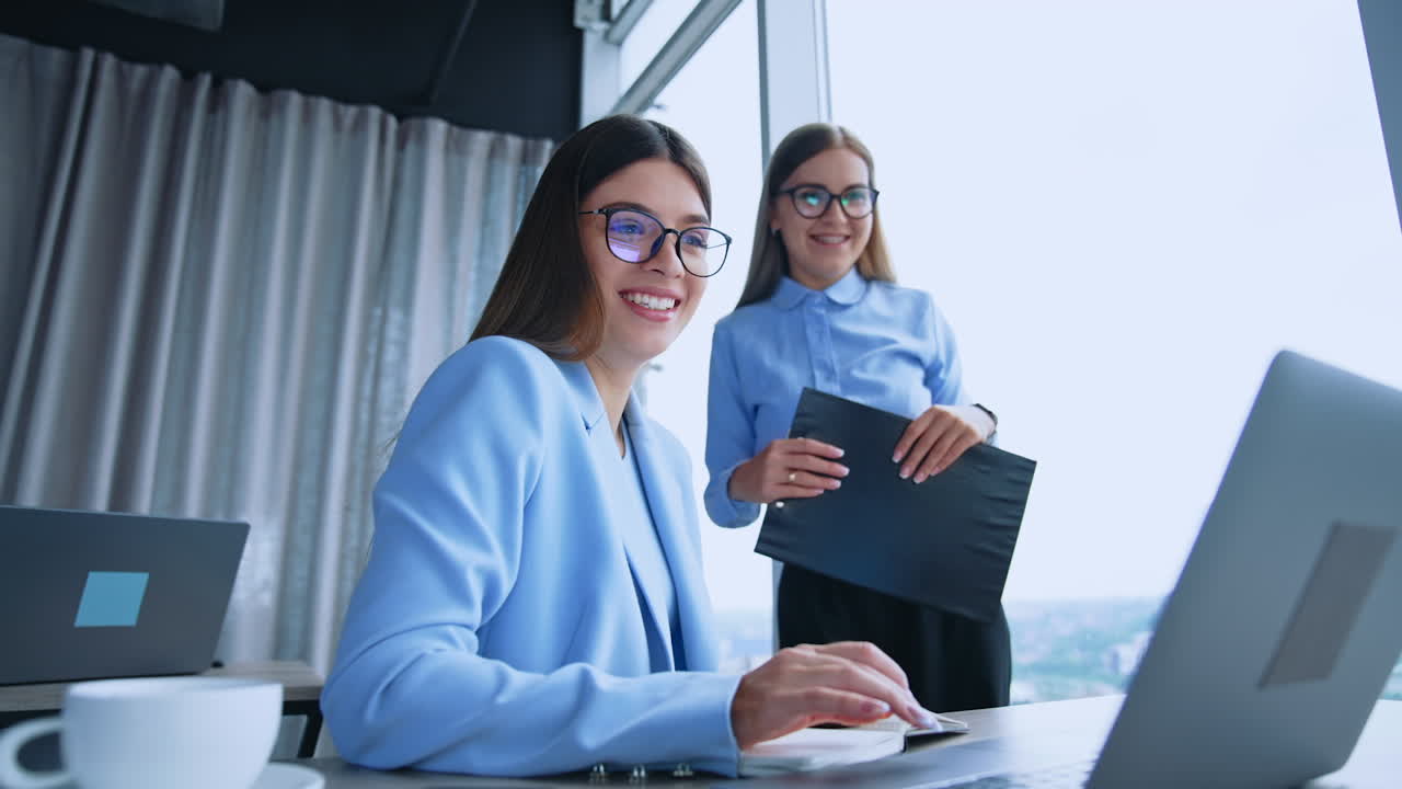 Happy resilient female employees in the modern office. Ladies look at the laptop screen smiling and getting surprised. Low angle view.