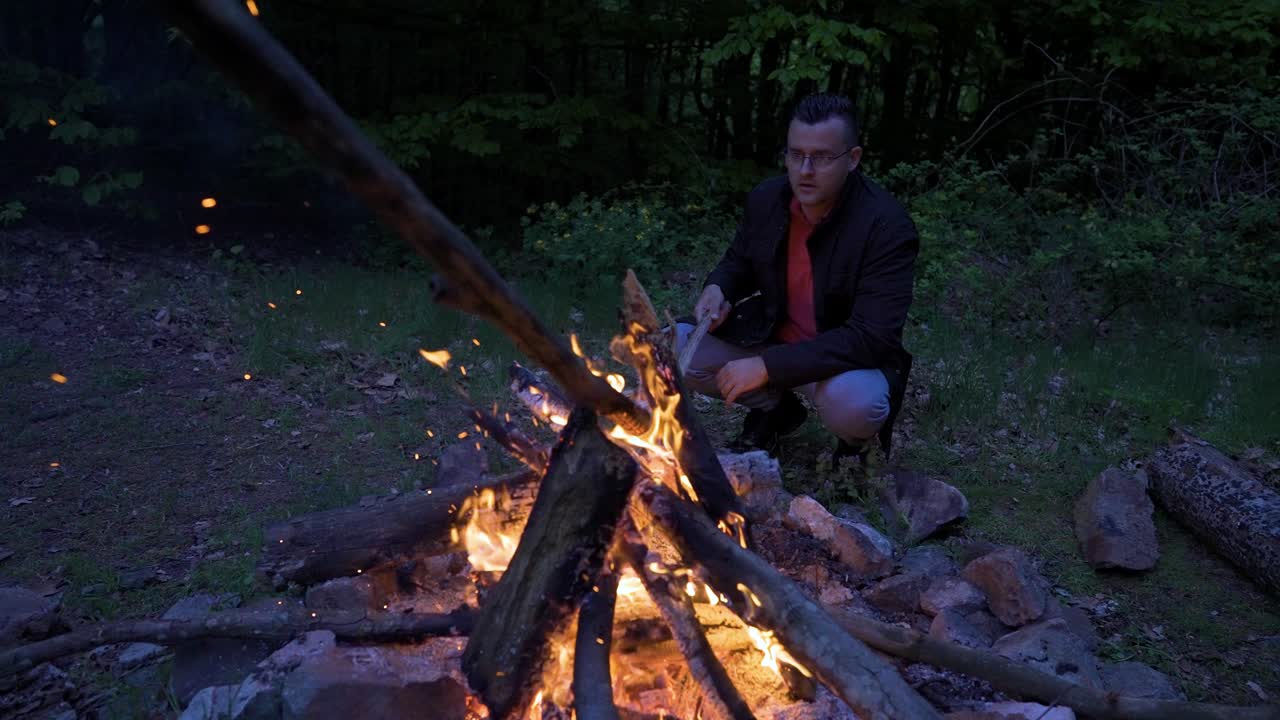 Campisten sitter ved bålet og legger mer ved på ilden for å holde flammene glødende, på en campingplass i Strandzha-fjellene i Bulgaria.