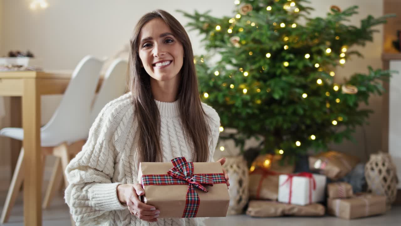 retrato de una mujer caucásica sonriente con un regalo de navidad en casa.