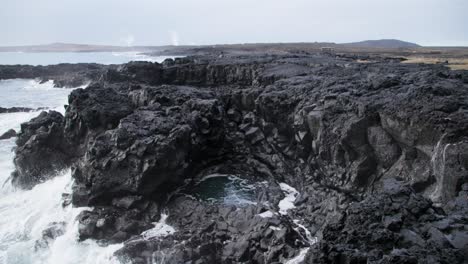 Schroffe-Basaltküste-Islands-Mit-Weißen-Schaumwellen,-Die-Spritzen,-Ozeanblasloch