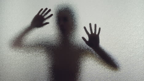 a female silhouette behind the frosted window slowly touches the glass