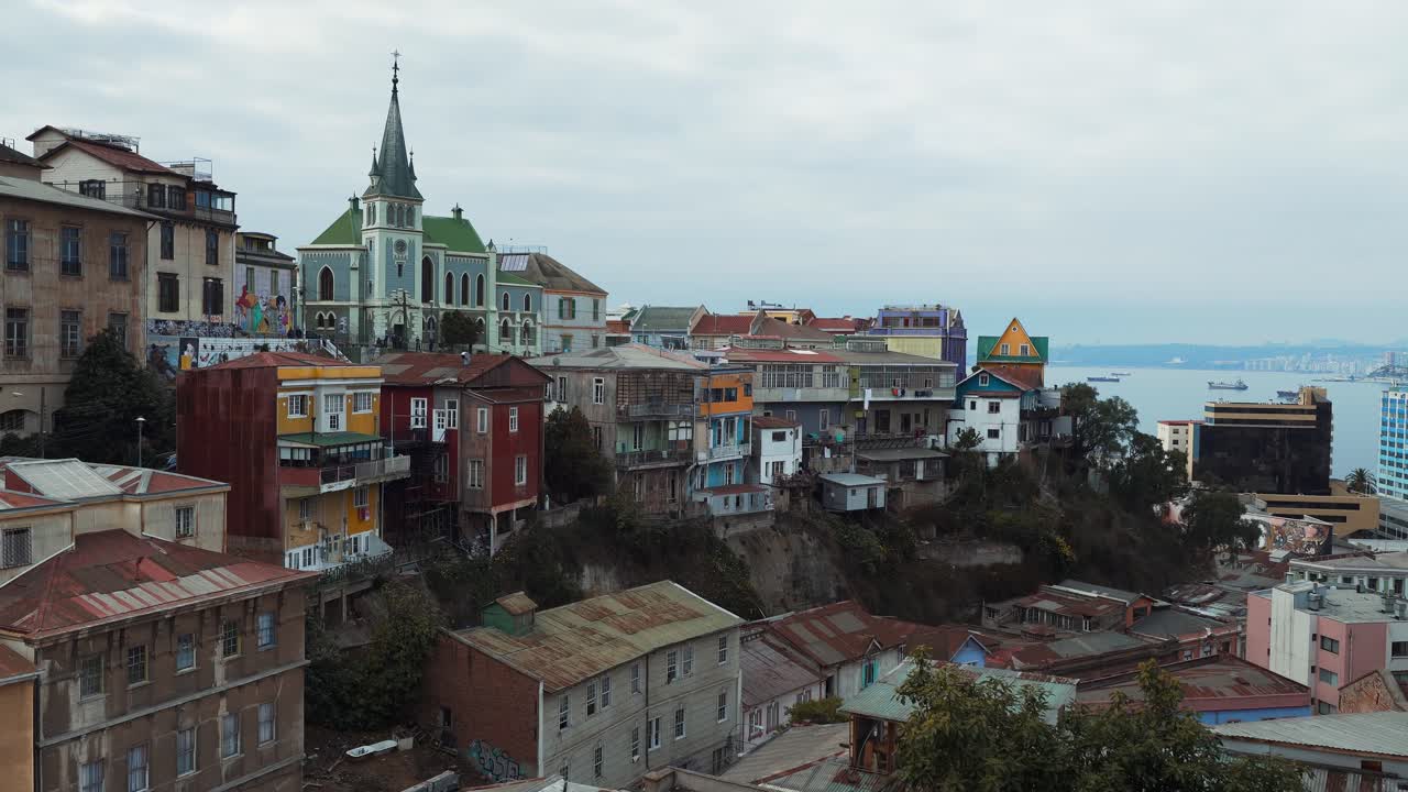 pan a la derecha de coloridas casas en las laderas y la iglesia luterana de cerro alegre en la ciudad de valparaíso, mar de fondo, chile