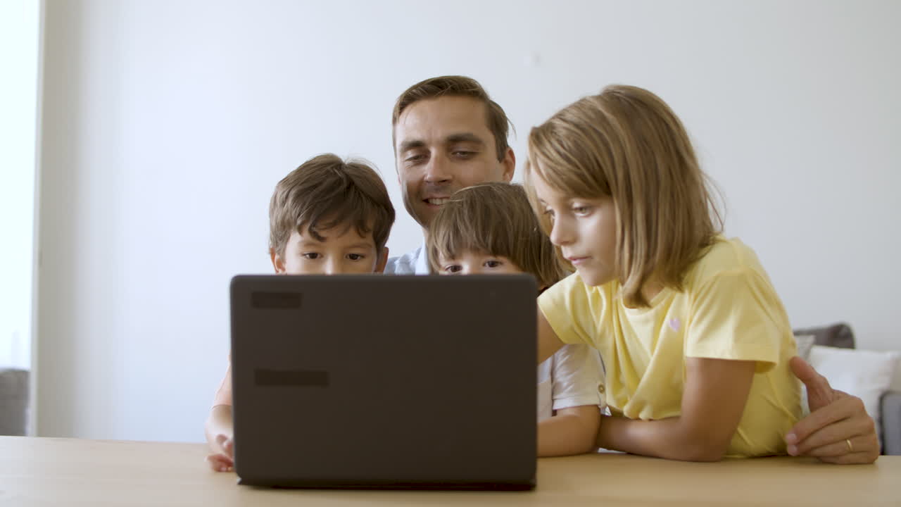 padre amoroso sentado en la mesa, abrazando a los niños y usando la computadora portátil