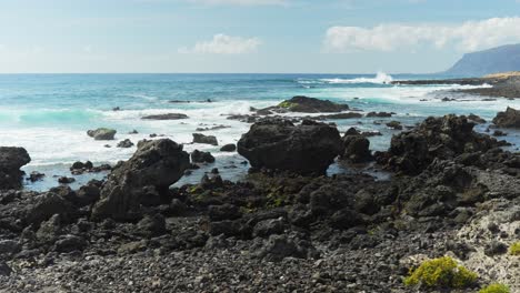 Panning-shot-at-the-sea-over-the-black-rocks-at-the-seashore-with-splashing-water,-dynamic