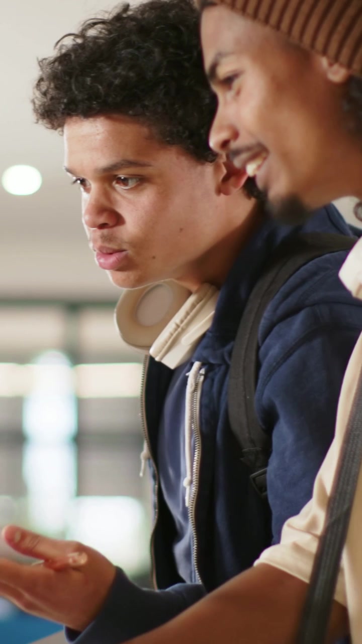 Vertical video: Leaning two students viewing offscreen cue at library in navy hoodie holding book