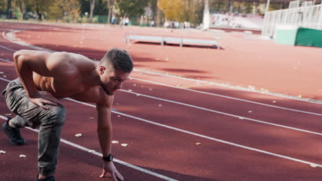 Shirtless athlete starts running on the stadium. Muscular male sprinter training on the outdoor athletics track. Sport and fitness concept.