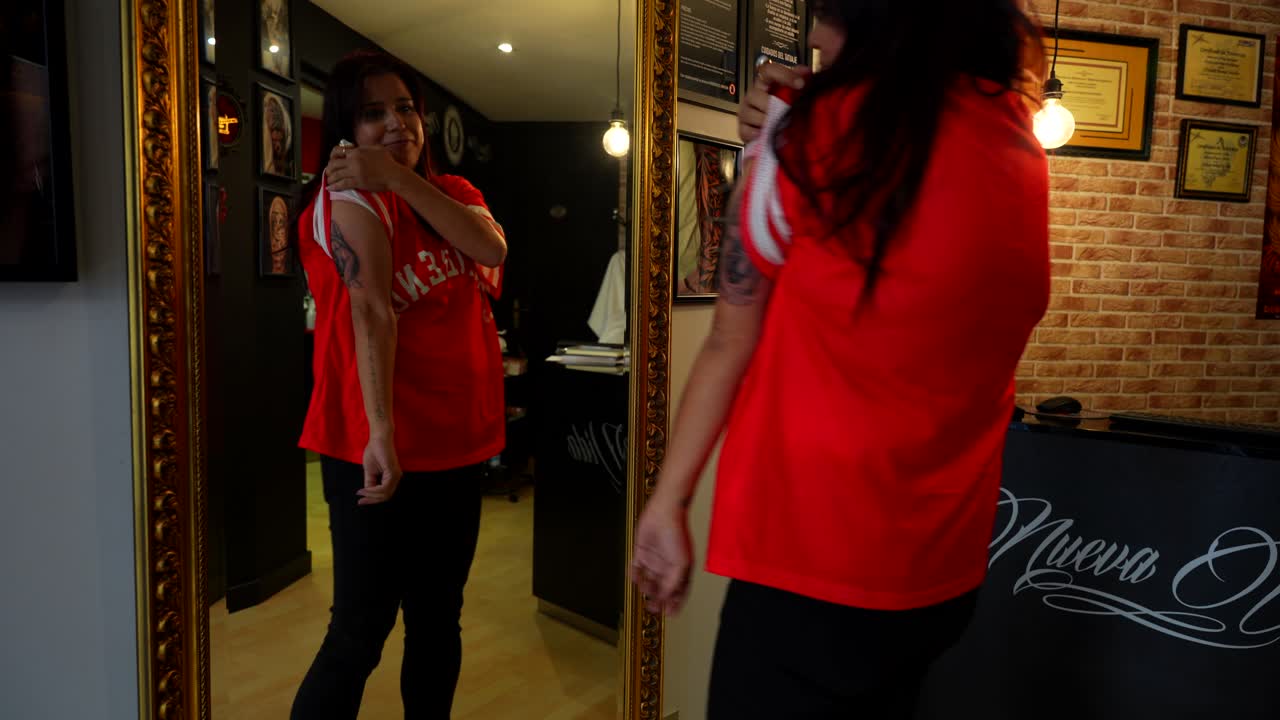 Woman looks at brand new tattoo on mirror, cries at end from excitement, tattoo studio