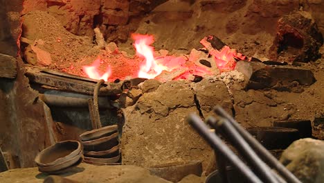 herrero trabajando en tazones con pinzas frente a un antiguo horno de fuego tradicional