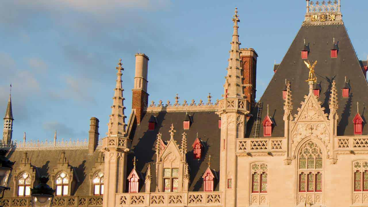 Camera slowly pans across ornate Gothic city hall facade in Bruges, golden hour sunlight