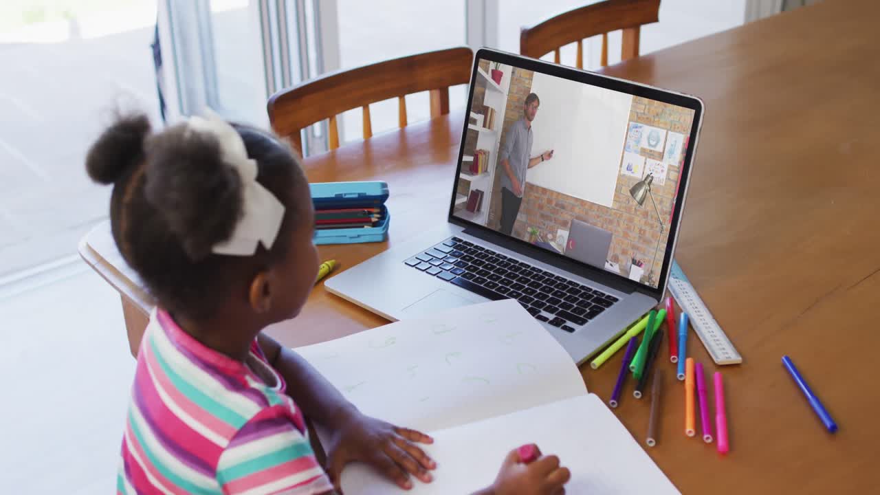 African american girl doing homework while having video call with male teacher on laptop at home