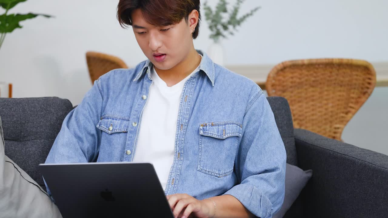 明るいリビングルームでラップトップで作業する若い男性のミディアムショット。