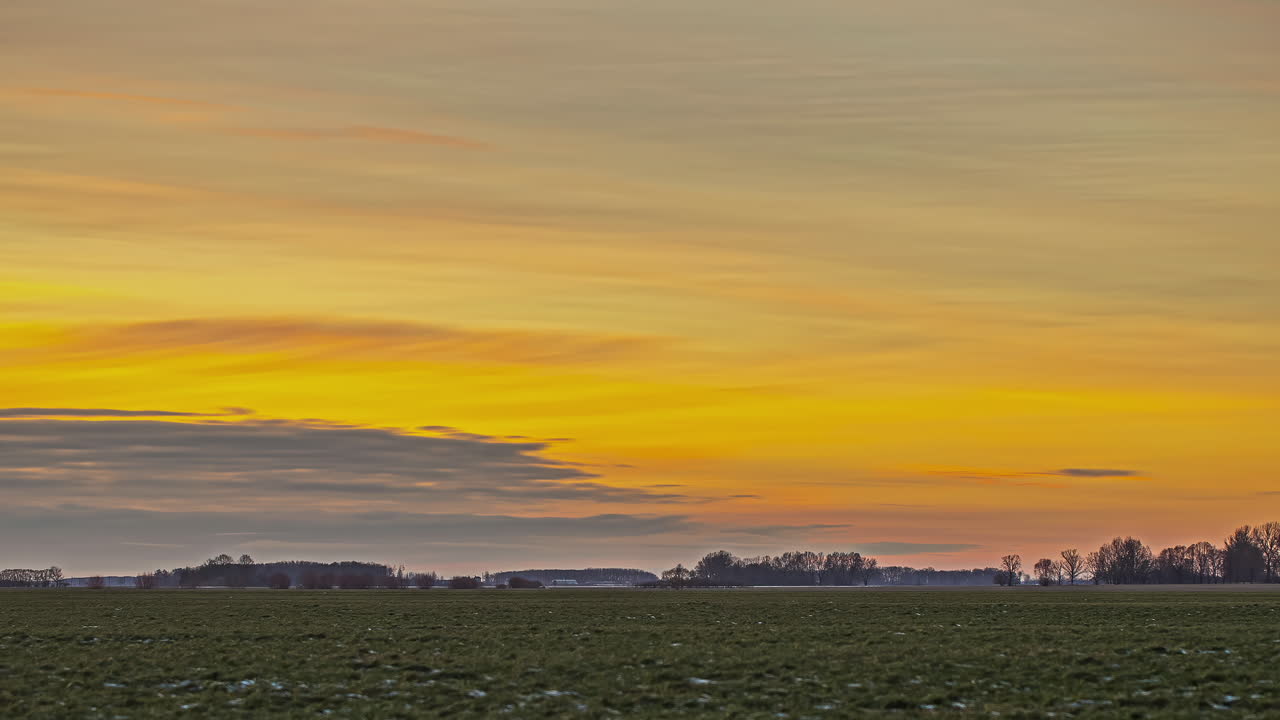 시골 풍경을 왼쪽에서 오른쪽으로 지나가는 구름과 함께 황금빛 오렌지색 일몰 하늘