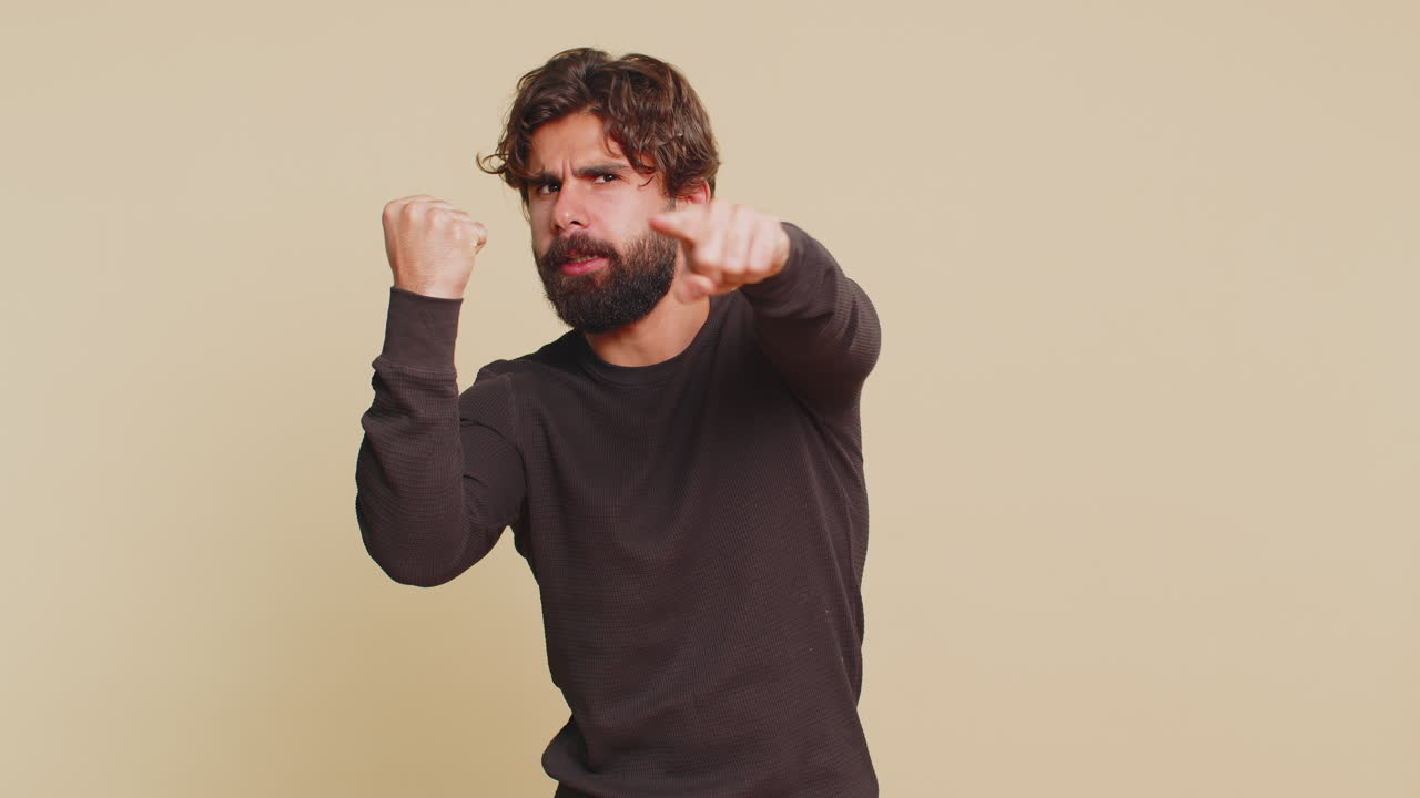 Portrait of furious young indian man hits fist on palm showing fight gesture over beige background