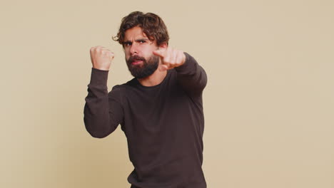 portrait of furious young indian man hits fist on palm showing fight gesture over beige background