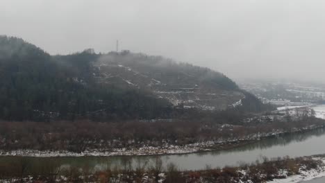 Paisaje-Invernal-De-Montaña-Con-Carretera-De-Montaña-Y-Río-Tranquilo-Que-Fluye,-Aéreo