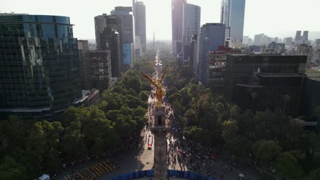 drone shot of angel of independence victory column monument on a roundabout on paseo de la reforma avenue, day of the dead parade celebration in downtown mexico street on sunny daylight