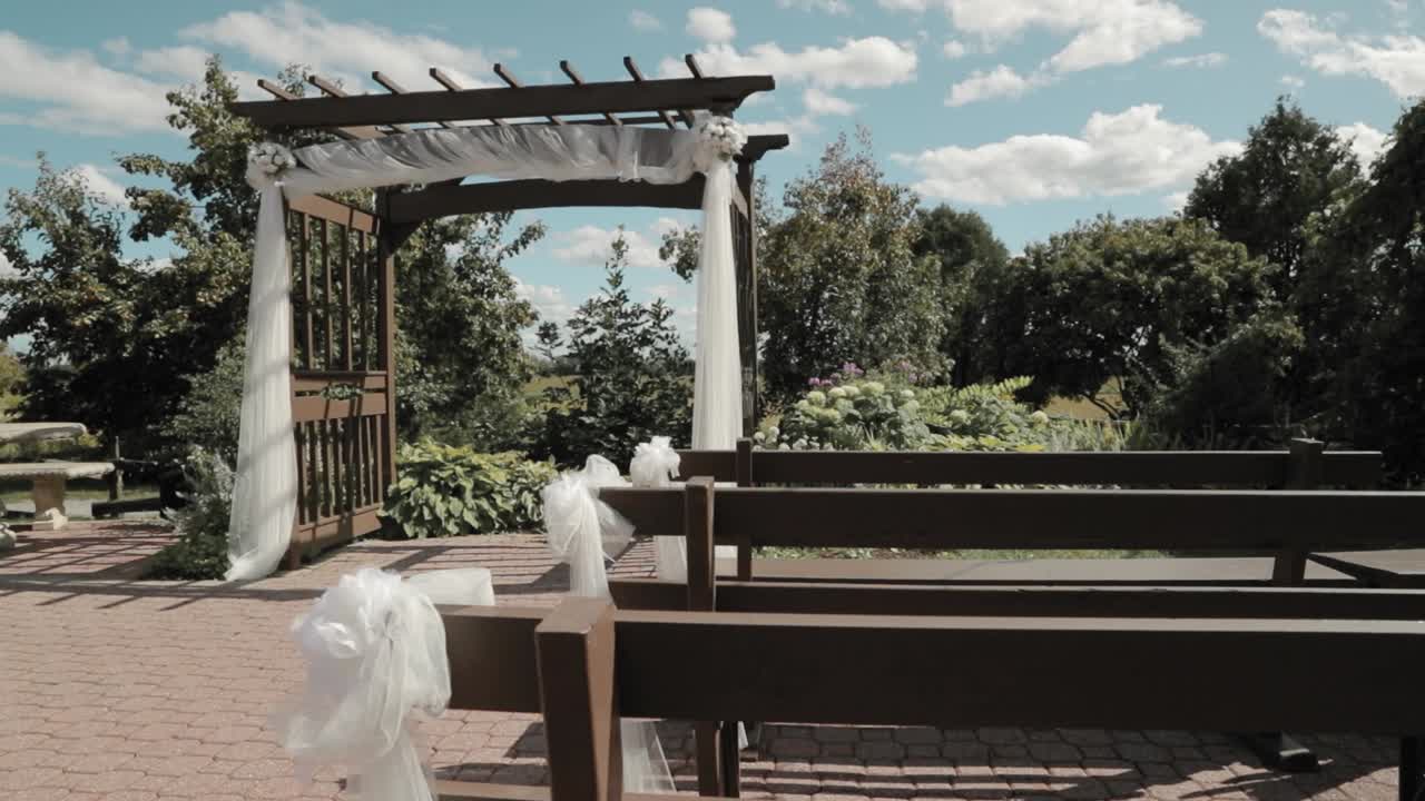 아름다운 야외 결혼식장, 멋진 푸른 흐린 하늘과 그 뒤에 멋진 정원이 있는 아름다운 아치형 통로의 좌석 벤치에서 촬영된 패닝 샷