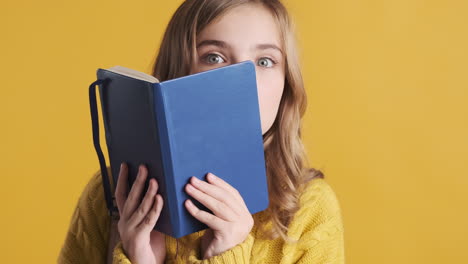 happy teenage caucasian girl student holding notebook in front of her head.